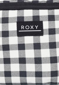 Czarno-biała tkanina w szachownicę z metką Roxy. Materiał ma teksturowany, tkany wygląd z wyraźnymi kwadratami w różnych odcieniach szarości.