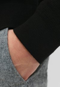 Crni pleteni manžet odjeće pored sivog uzorka tkanine s džepom. Tekstura je glatka, a boje se oštro kontrastiraju.