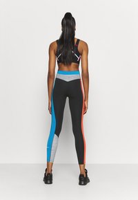 Czarne legginsy sportowe z niebieskimi, pomarańczowymi i szarymi wstawkami; dopasowany krój; zestawione z czarnym biustonoszem sportowym z kontrastowymi szwami.