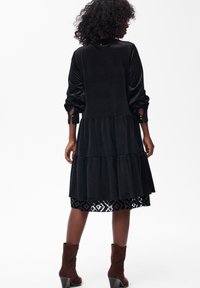 Czarna aksamitna sukienka z falbaniastą spódnicą, długimi bufkami i koronkowym wykończeniem u dołu. Noszona z brązowymi botkami za kostkę.