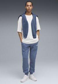 Blå bomulds hoodie båret over en hvid t-shirt, parret med blå sweatpants med sidelommer og hvide sneakers.
