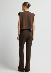 Bruine cropped trui met cap sleeves, gecombineerd met bruine op maat gemaakte broek, met een gladde textuur en een getailleerd ontwerp.