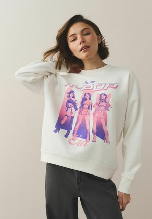 Young woman wearing a white sweatshirt with a purple-pink graphic of three stylized women and the text "In my POP Era."