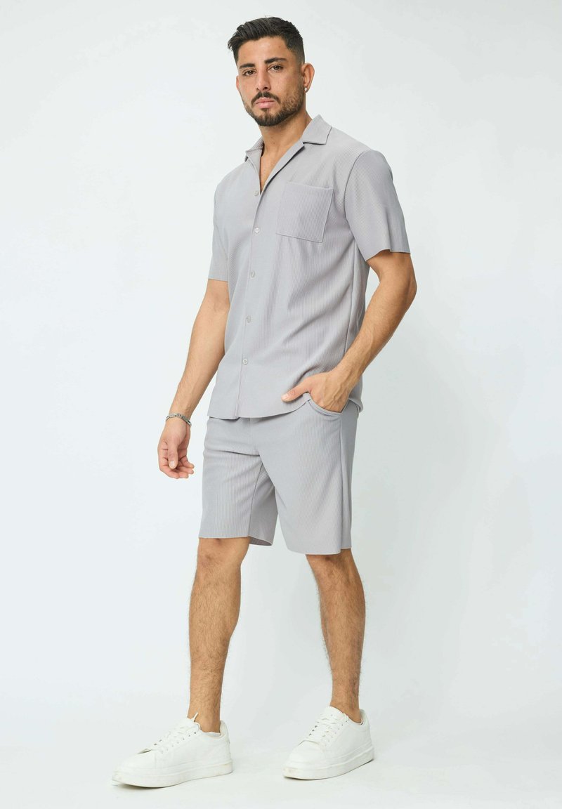 Chemise grise à manches courtes avec une poche poitrine, assortie à un short. Les deux présentent une texture côtelée, complétée par des baskets blanches.