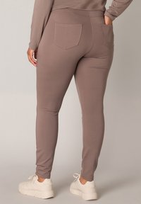 Bruine leggings met een gladde textuur, een getailleerd ontwerp en twee achterzakken, gecombineerd met witte sneakers voor een casual uitstraling.