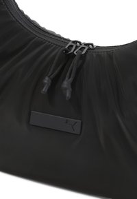 Sort nylon taske med en samlet design, der har to lynlåse og sorte snoretræk. En mat sort logoblade er centreret på forsiden.