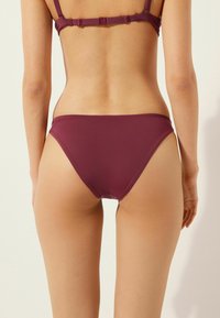 Bordeauxfarbenes Bikini-Set mit verstellbaren Trägern und tief sitzenden Höschen. Glatte Textur, minimalistisches Design und keine sichtbaren Metallteile.