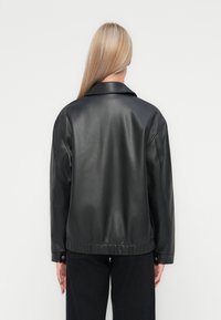 Veste en cuir noir avec une coupe décontractée, large col et ourlet élastique. Texture lisse, poignets boutonnés et sans motifs visibles.