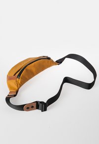 Heuptas in mosterdgeel stof met een zwarte rits, accenten van bruin leer en een verstelbare zwarte band. Gebogen vorm met een slank ontwerp.
