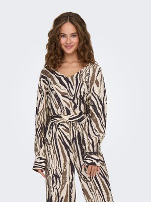 Giovane donna con capelli ricci che indossa una maglia a maniche lunghe e pantaloni abbinati con motivo astratto a zebra beige, marrone e nero, sorridente.