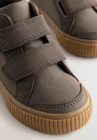 Brązowe buty na rzepy z textured górą i wyściełanym kołnierzem. Posiadają gumową podeszwę z poziomymi rowkami dla lepszej przyczepności.