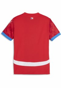 Punainen urheilupaita, jossa on lyhyet hihat sinisillä yksityiskohdilla, valkoinen raita alaosassa ja lippuapplikointi takana.