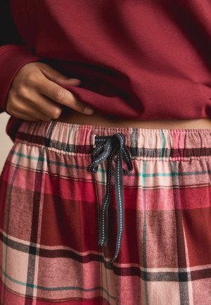 Bas de pyjama à carreaux rouges et roses avec une taille élastique et un cordon noir. Tissu doux avec un motif à carreaux et des couleurs contrastées.