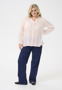 Light pink button-up blouse with a textured pattern, long sleeves, and a relaxed fit, paired with dark blue wide-leg jeans and black flats.