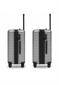 Deux valises rigides argentées avec des poignées noires extensibles, quatre roues et des serrures à combinaison latérales, présentées côte à côte sur un fond blanc.
