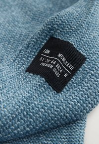 Dzianina o niebieskim kolorze z teksturowaną powierzchnią, z czarną metką z tekstem i współrzędnymi, wszytą w tkaninę.