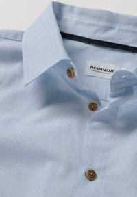 Lichtblauw overhemd met knopen, gemaakt van een gestructureerde stof, met een puntige kraag en twee bruine knopen op de knopenlijst, voorzien van een label van hessnatur.