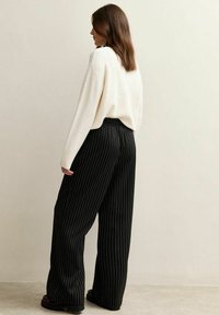 Pantalones de pierna ancha a rayas negras con cintura elástica, combinados con un suéter de punto oversized color crema, vistos desde atrás.