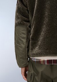 Tummanvihreä fleece-takki, jossa on tekstuuri pinta, sisältää sileät, tikatut hihat ja kerroksellisen paidan, jossa on ruutukuosi alhaalla.