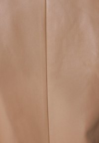 Beige læderstof med en glat overflade og en lodret søm, der løber ned ad midten. En diskret glans fremhæver dens kvalitet.