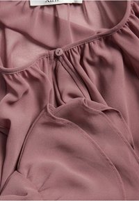 Ljusrosa chiffonblus med mjuka veck, rund halsringning och knappstängning fram. Slät textur och flödande design.