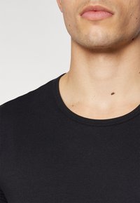 T-shirt noir à manches courtes avec col rond. Tissu lisse et extensible avec des coutures minimales, montrant un gros plan du col et du haut du torse.