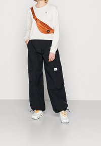 Cropped cream long-sleeve top with a logo, black wide-leg cargo pants, and white sneakers with orange accents. Brown crossbody bag.