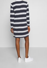 Langärmliges Kleid mit maritimen und weißen Streifen, knielang mit lockerem Schnitt, kombiniert mit weißen Sneakern. Einfaches Design, weicher Stoff.