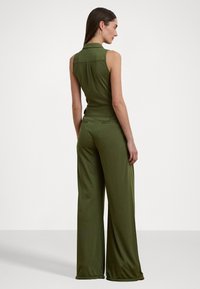 Olivgrön jumpsuit med ärmlös design, krage, vida byxor och sidofickor, tillverkad av ett mjukt, stretchigt tyg.