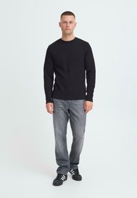 Črna dolga majica z okroglo ovratnico, v kombinaciji s sivo denimom in črnimi športnimi čevlji s tremi belimi črtami.