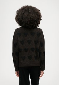 Καφέ �πουλόβερ με μαύρο σχέδιο καρδιάς, μαλακή υφή, στρογγυλή λαιμόκοψη και μακριά μανίκια. Τα χαρακτηριστικά του σχεδιασμού περιλαμβάνουν χαλαρή εφαρμογή και ριμπ μανσέτες.