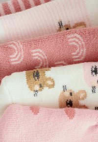 Une pile de chaussettes en tricot pliées en rose et blanc, ornées de visages d'ours et de motifs géométriques.