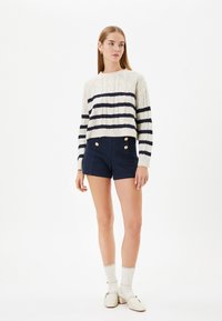 Crème en marine gestreepte trui met kabelbrei ontwerp, gecombineerd met hoge taille marine shorts met gouden knoopaccents.