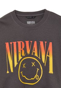 T-shirt in cotone grigio con la scritta "NIRVANA" in un gradiente che va dall'arancione al giallo sopra un design di faccina sorridente gialla con gli occhi incrociati.