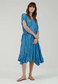 Blauwe, lichte jurk tot de knie met een gestructureerde, gekreukte afwerking. Voorzien van korte mouwen, een v-halslijn en gouden hardwareaccenten.