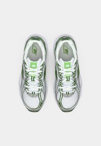 Valge ja roheline paar New Balance jooksujalatseid valgete paeltega, vaadatuna ülalt tavalise valge tausta pealt.