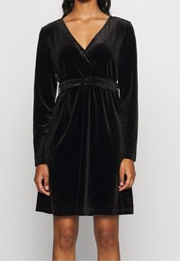 Svart sammet omslagsklänning med långa ärmar, djup V-ringning och ett matchande bälte vid midjan. Slät textur och klassisk design.