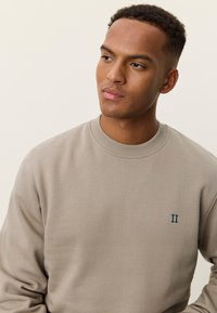 Φωτεινό μπεζ φούτερ με ριμπ λαιμόκοψη, με κεντητό σκούρο πράσινο "II" στο στήθος και απαλό ύφασμα.