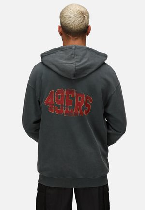 Sudadera gris con un gran gráfico desgastado de "49ERS" en rojo y amarillo en la parte posterior, con capucha ajustable y puños de canalé.