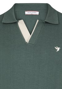 Tmavě zelené pletené polo tričko s béžovým výstřihem do V. Má límec a vyšitý bílý pták logo na levé straně hrudi.