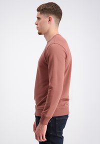 Sudadera de cuello redondo marrón hecha de algodón, con mangas largas, puños acanalados y un corte regular. Llevada con jeans de mezclilla oscura.