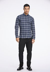 Camisa de cuadros en azul marino y gris de manga larga con cuello abotonado, combinada con pantalones negros ajustados y zapatos negros de cordones.