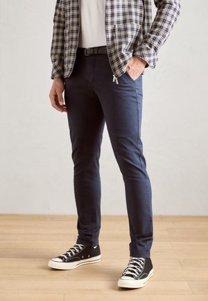 Morske slim-fit hlače iz bombaža, z gladko teksturo, stranskimi žepi in v kombinaciji s črnimi visokimi superge.