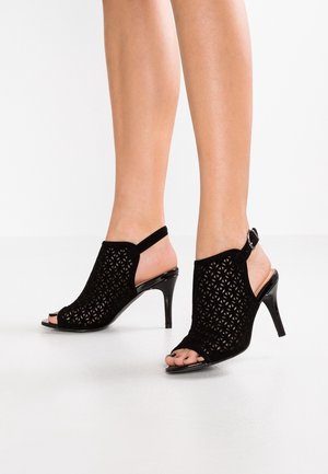 Sorte åbne hæle med perforeret design, blødt velourmateriale og stilettohæl, der har ankelrem med spænde.