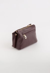 Burgundowa skórzana saszetka z złotym zamkiem błyskawicznym i kieszonką. Miękka tekstura, prostokątny kształt i kompaktowy design do przechowywania.