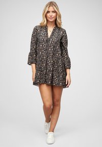 Robe noire à fleurs avec un décolleté en V, de longues manches en cloche et un ourlet à volants superposés. Présente de petites fleurs colorées et un tissu léger.