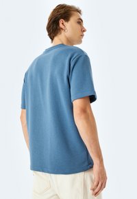 Blå bomullströja med korta ärmar och rund halsringning. Mjuk textur, rak passform och minimal sömdetalj i fållen.