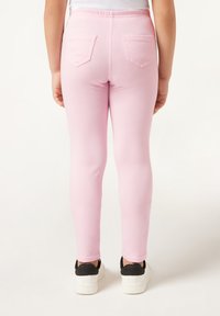 Leggings rosas con un diseño ajustado, que cuentan con dos bolsillos traseros y una cinturilla elástica, combinados con zapatillas blancas y detalles negros.
