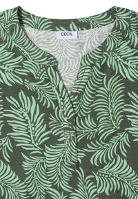 Chemise verte avec un motif de feuilles tropicales vert clair, col rond avec une courte patte de boutonnage et une étiquette de marque CECIL visible à l'intérieur du col.