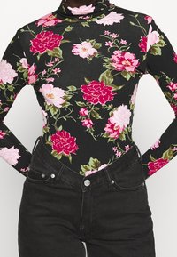 Svart turtleneck bodysuit med rosa och röda blommönster, lång ärm och en figurnära design, kombinerad med högmidjade svarta jeans.